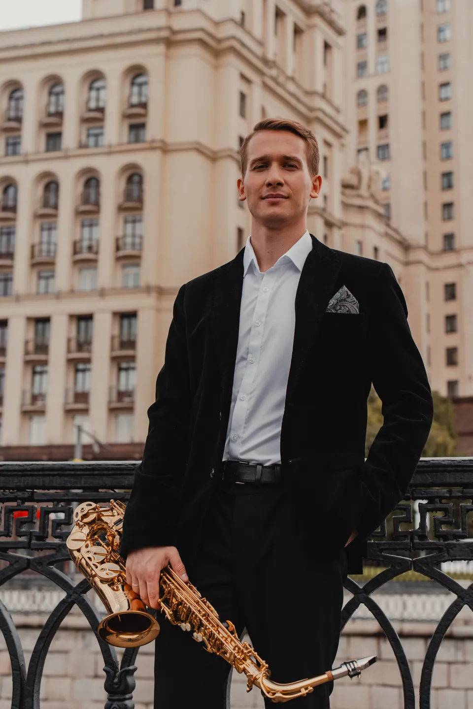 Саксофонист Лео в чёрном костюме на фоне московской архитектуры