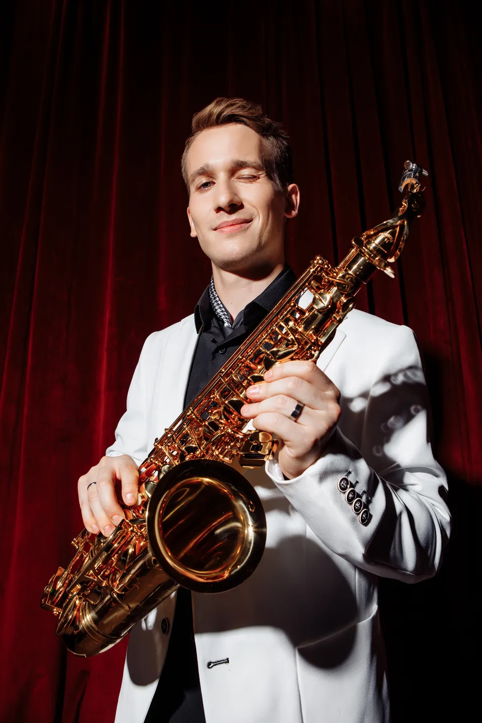 Leo Sax с саксофоном в белом пиджаке у красной кулисы